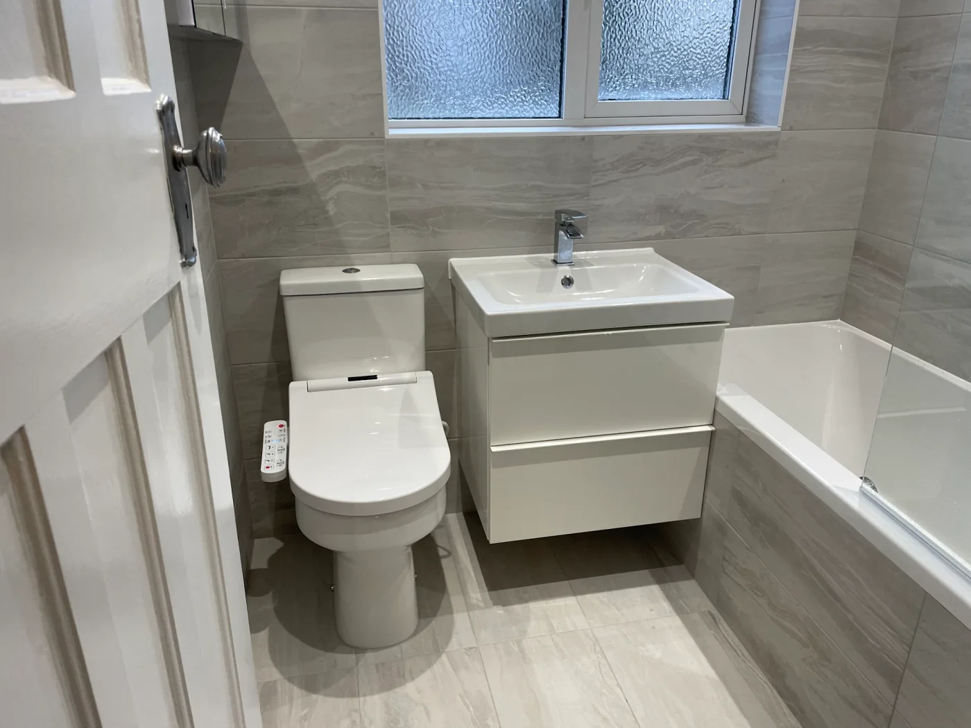 Grey tiled family bathroom with bath, vanity and toilet
