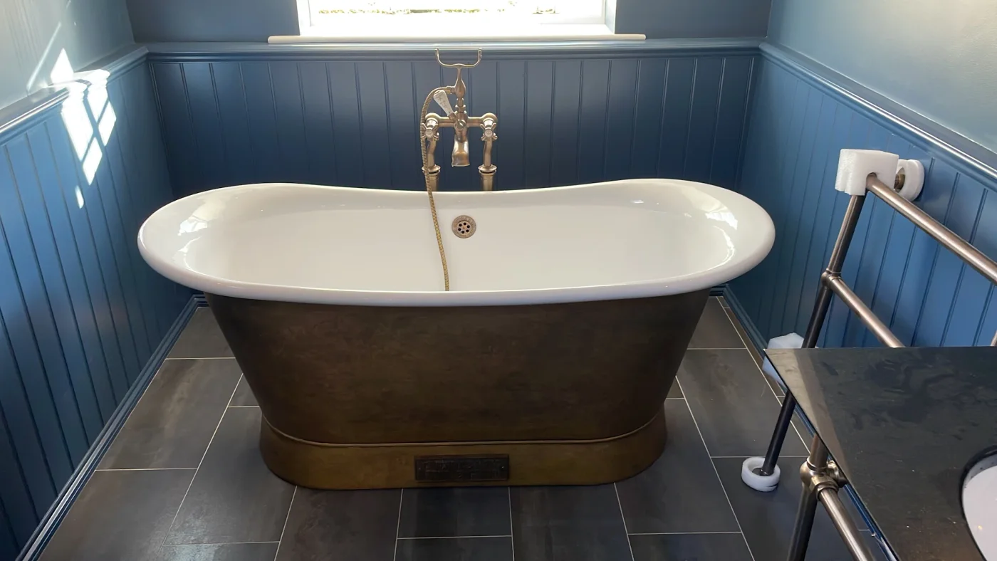 Freestanding brass-coloured bath against blue wall panelling