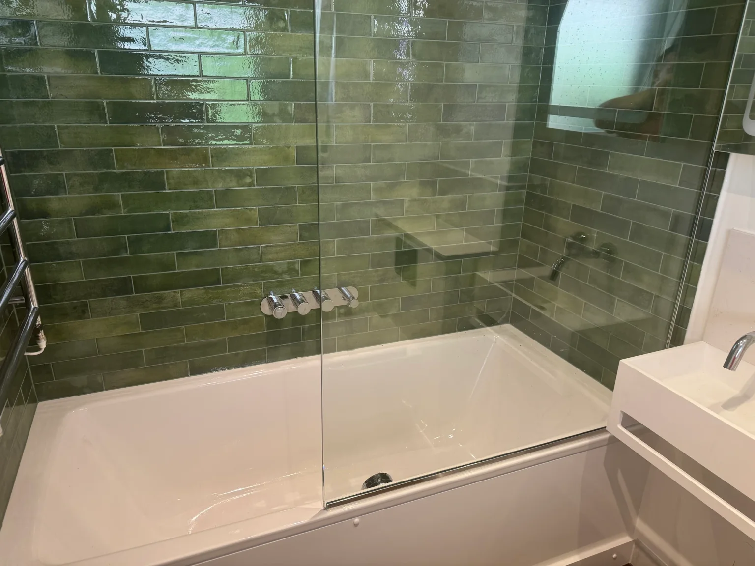 White bath and glass screen surrounded by glossy green wall tiles