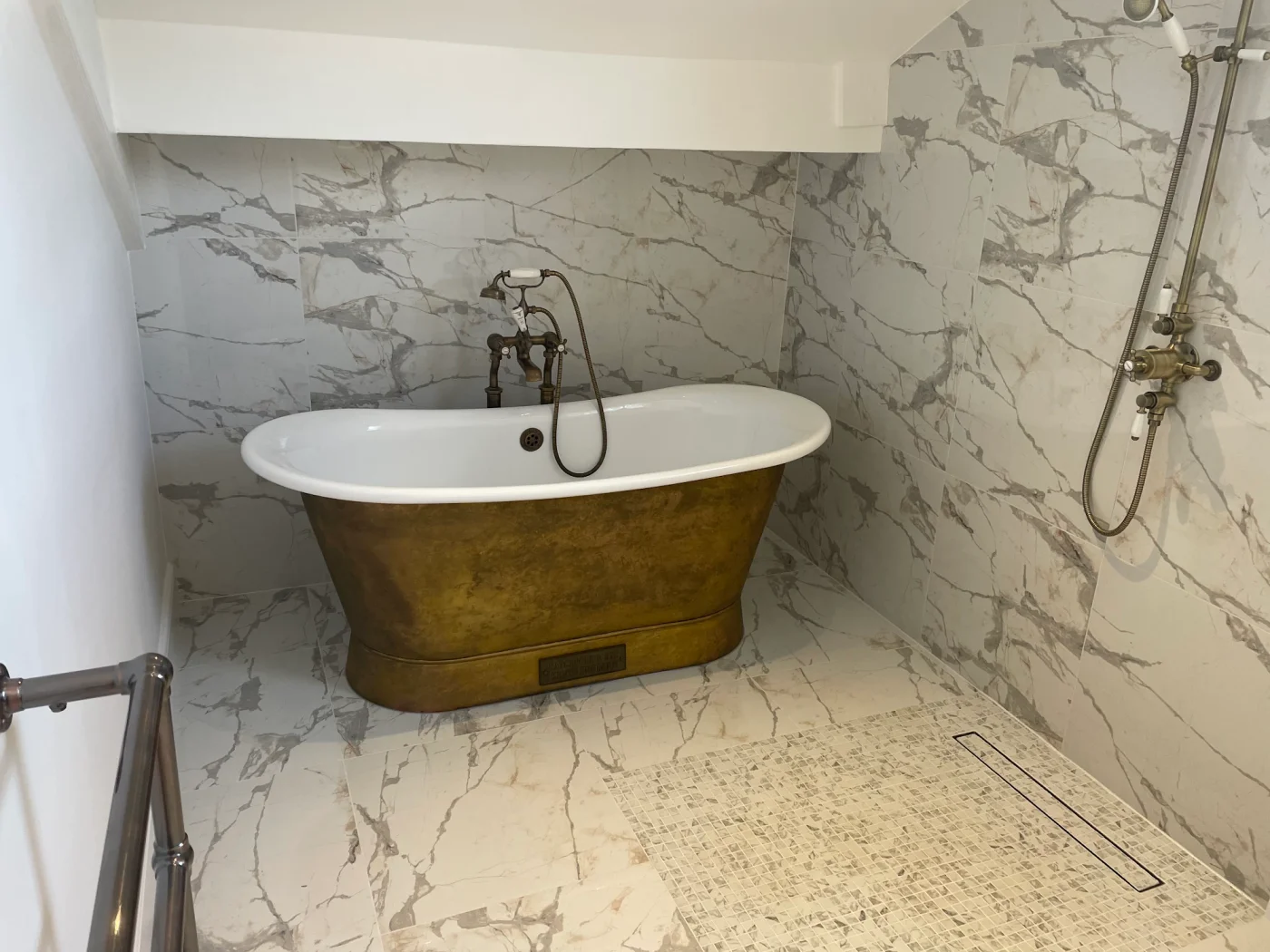 Brass-coloured roll-top bath beside a glass shower