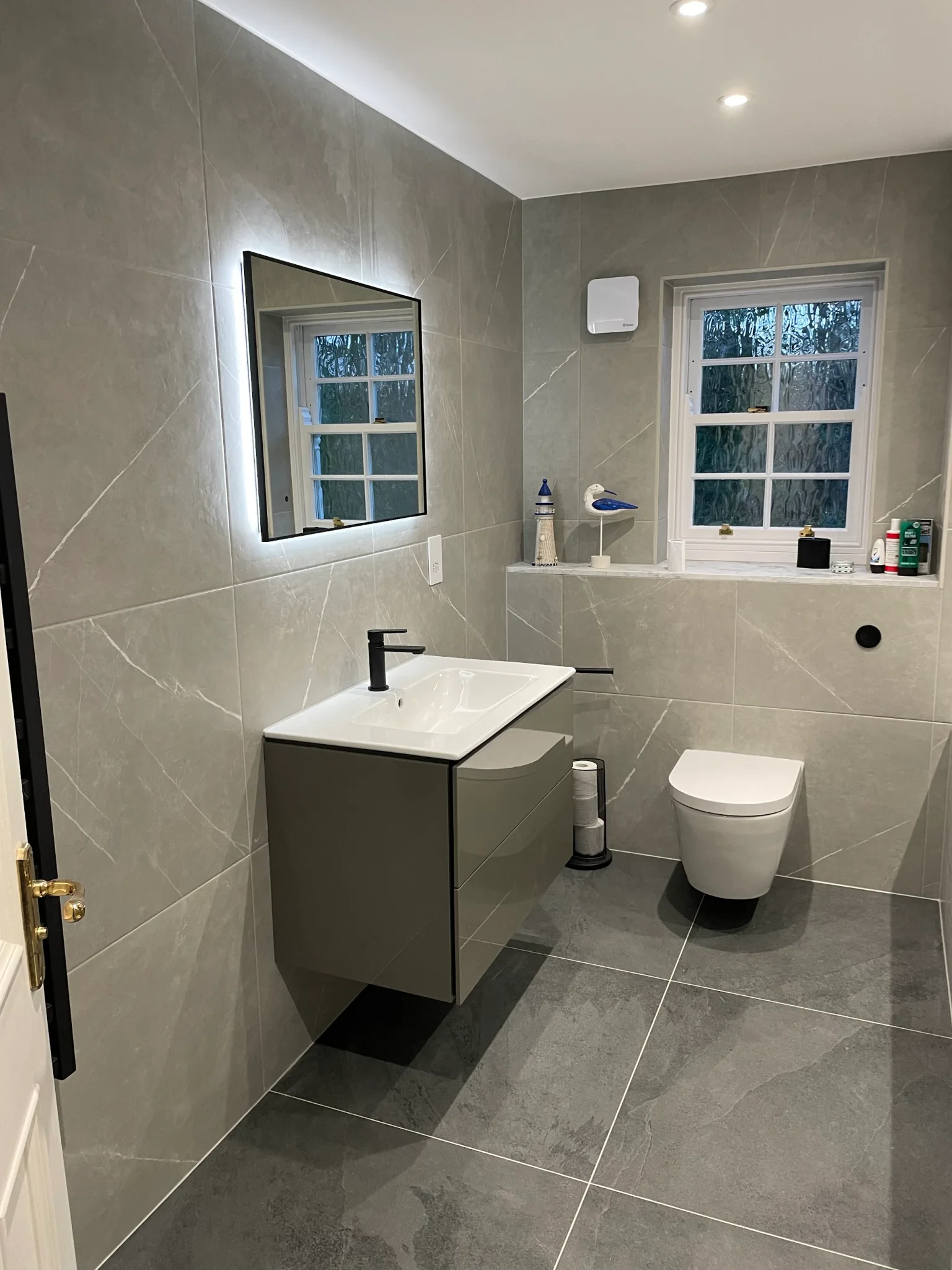 Wall-hung vanity and toilet with black fittings and large-format grey floor tiles
